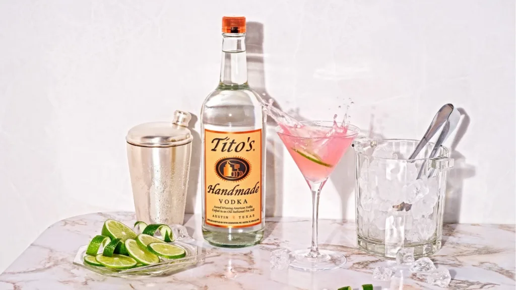 Vodka bottle with cocktail, shaker, ice bucket, and limes.